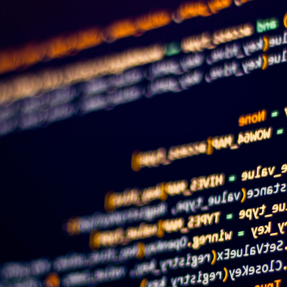 Nahaufnahme eines verschwommenen Computerbildschirms, auf dem Codezeilen in verschiedenen Farben vor einem dunklen Hintergrund angezeigt werden.
